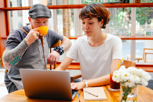 Two business owners hold a discussion while using their laptops.